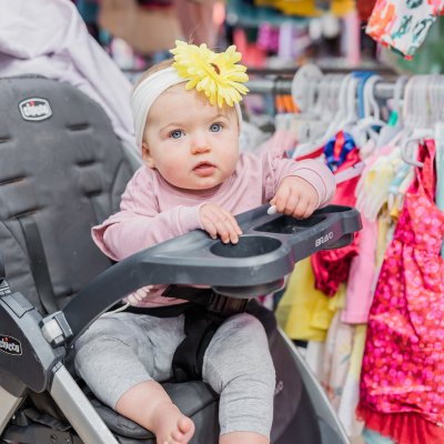 A baby girl sits in a stroller with a yellow daisy on her headband.
